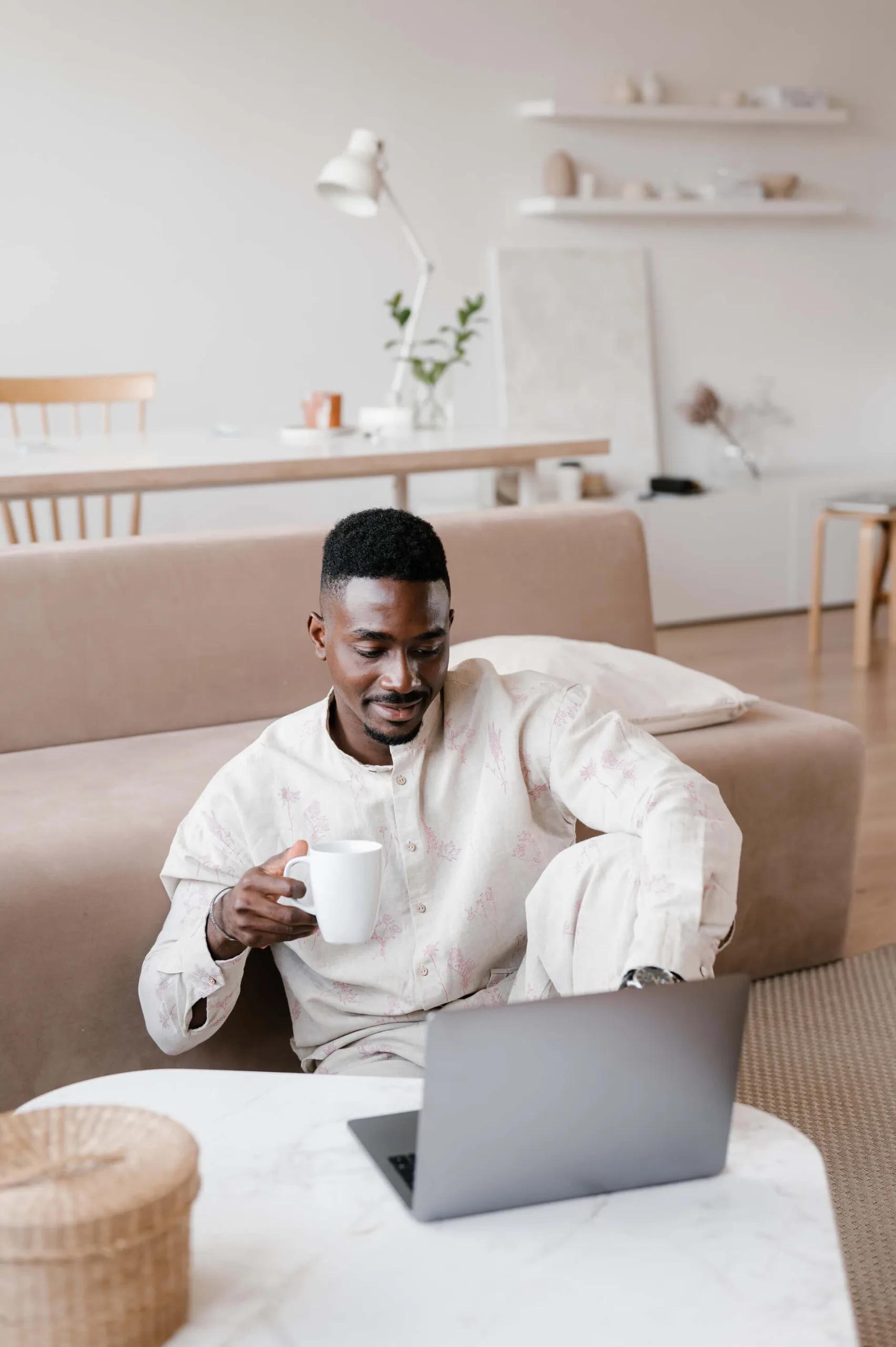 A man drinking a cup of coffee while working on his laptop